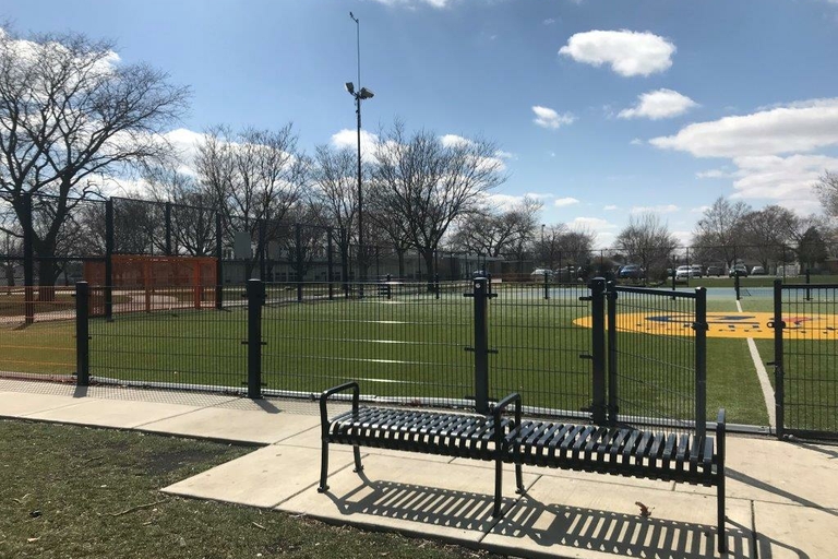 Fenced-in turf athletic field with a park bench on a sunny day.