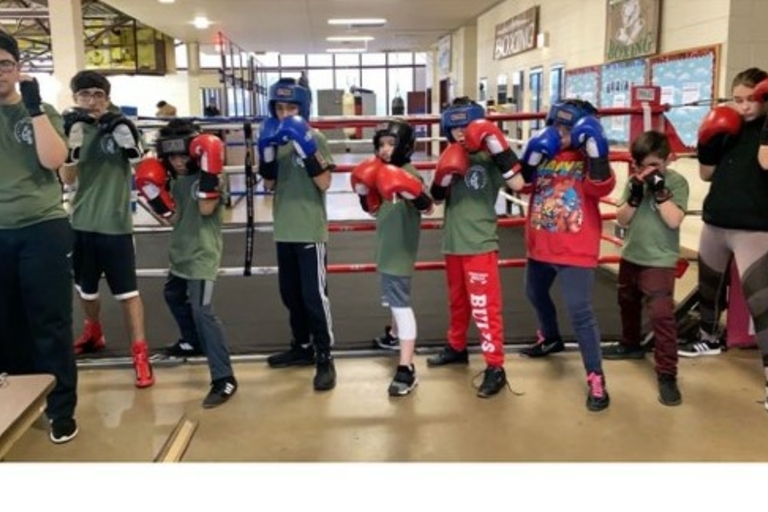 Young boxers pose by the ring, wearing boxing gloves and headgear.
