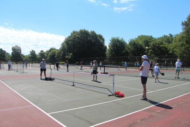 People playing pickleball on outdoor courts on a sunny day.
