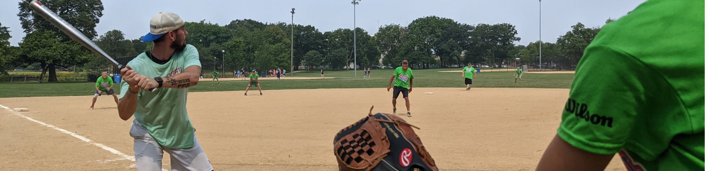Softball batter up at bat with fielders in the background.