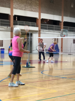 Seniors playing badminton in a gym.
