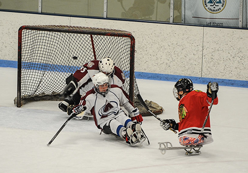 Sled hockey players battle for the puck in front of the net.