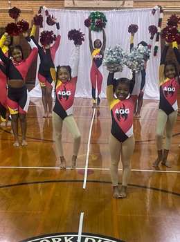 Young cheerleaders pose on basketball court, holding pom-poms.