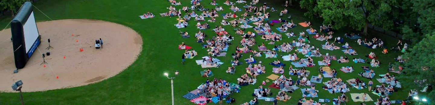 An aerial photograph of people on blankets watching a movie on an inflatable outdoor screen in a park.