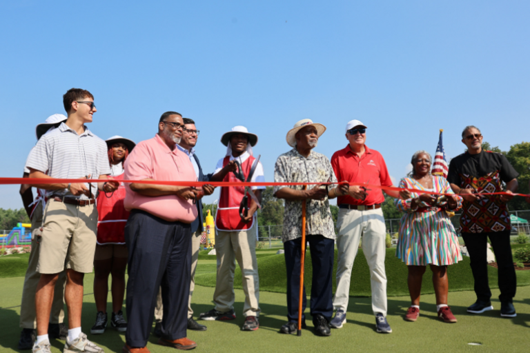 Group of people cutting a red ribbon at a grand opening ceremony.