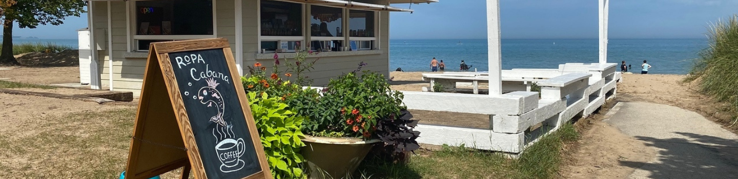 Beachside cafe with chalkboard sign and people swimming in the lake.