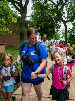 Camp counselor walks hand-in-hand with two smiling girls.
