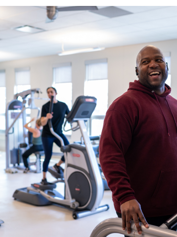 Smiling man on treadmill, others exercising in background. Gym setting.