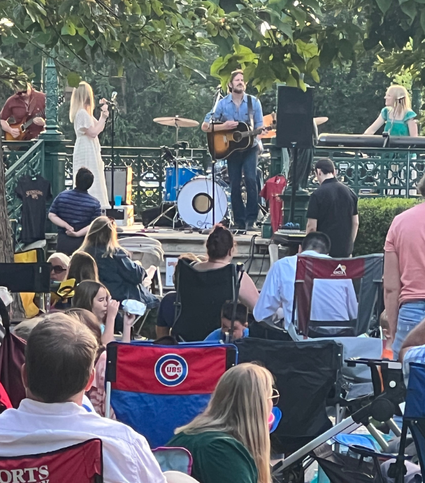 Outdoor concert with band on stage and people in lawn chair watching in a Chicago park.