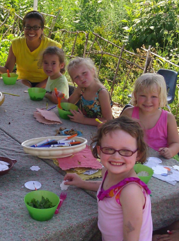 Children and a teacher crafting at a table outdoors.