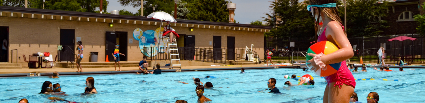 Crowded public swimming pool on a sunny day; patron stands poolside.