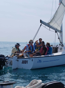 Smiling sailors wave from a small sailboat named "Judy".