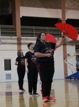 Three women demonstrate Tai Chi fan form in a gymnasium.