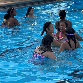 Group of girls playing together in a bright blue swimming pool.