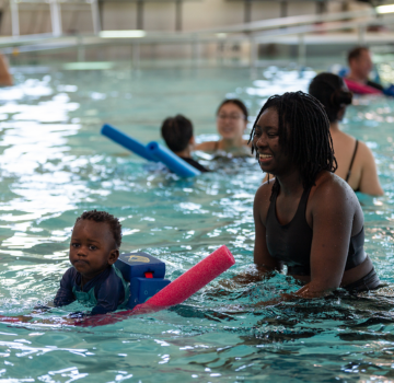 Smiling woman and toddler with flotation device in pool during swim class.
